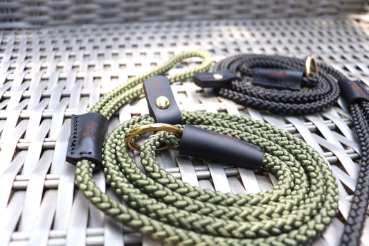 Green braided dog leash with black leather ends on a wicker surface