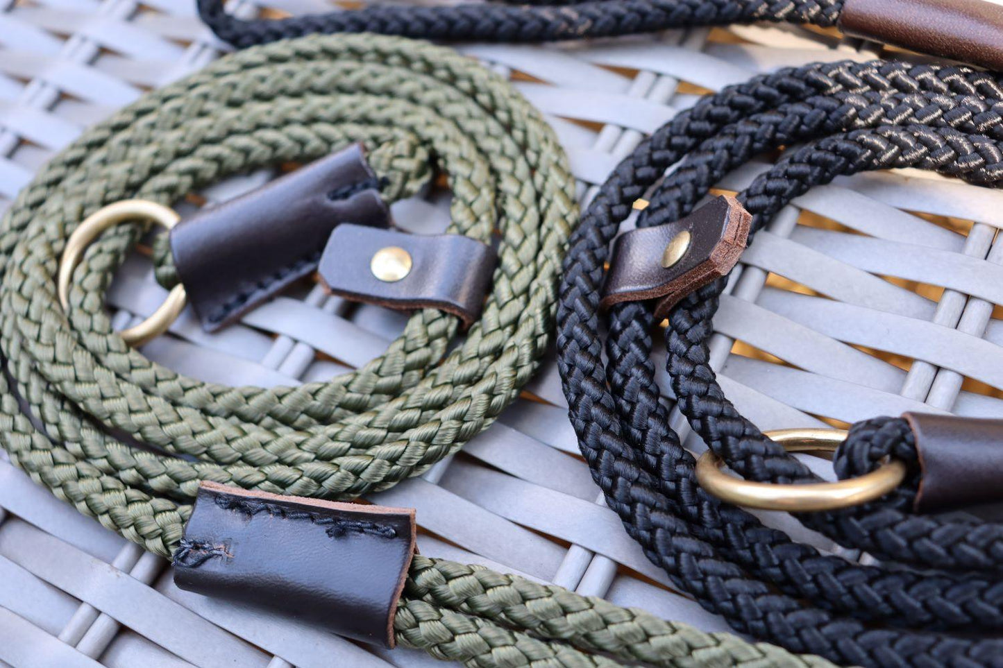 Two slip leads, one olive green and one black both with brown leather stopper and bindings and a brass ring and rivet.