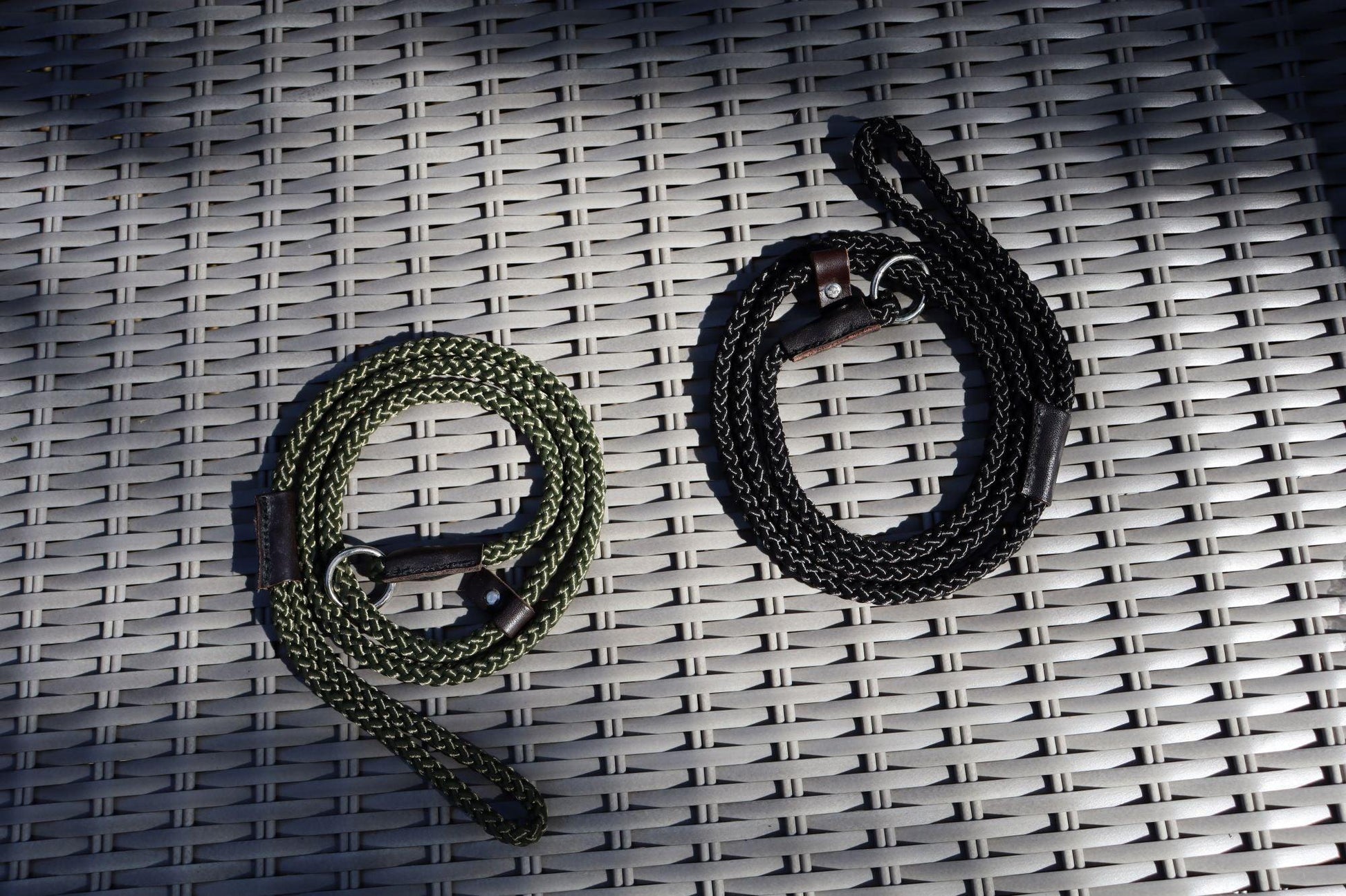 An olive green and a black slim slip lead in low lighting on a rattan furniture from a birds eye view angle.