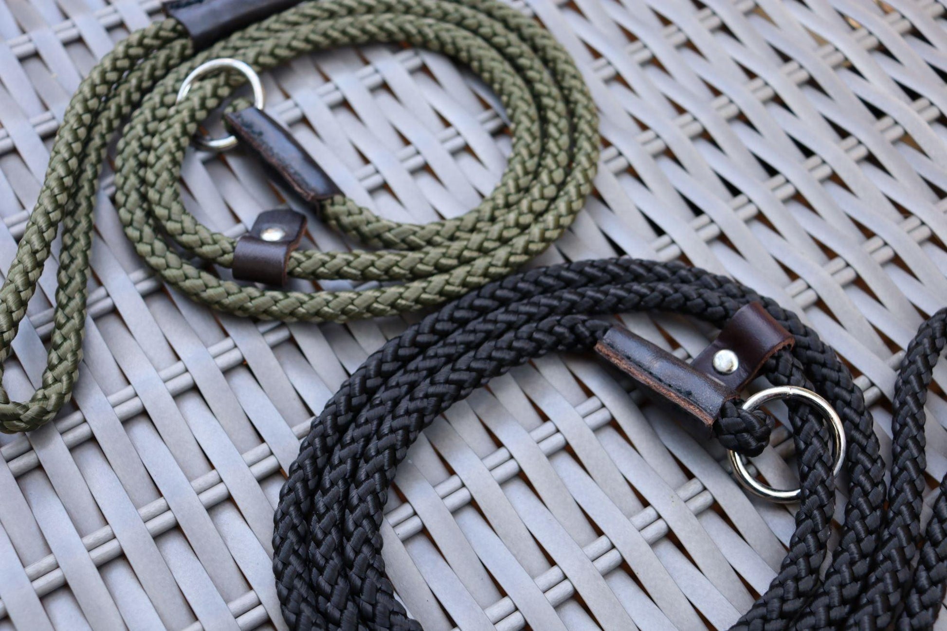 A close up on the black thin nickel slip lead with the olive green in the background. It is showing the tight braid and the leather stopper and binding around the handle and ring loop.