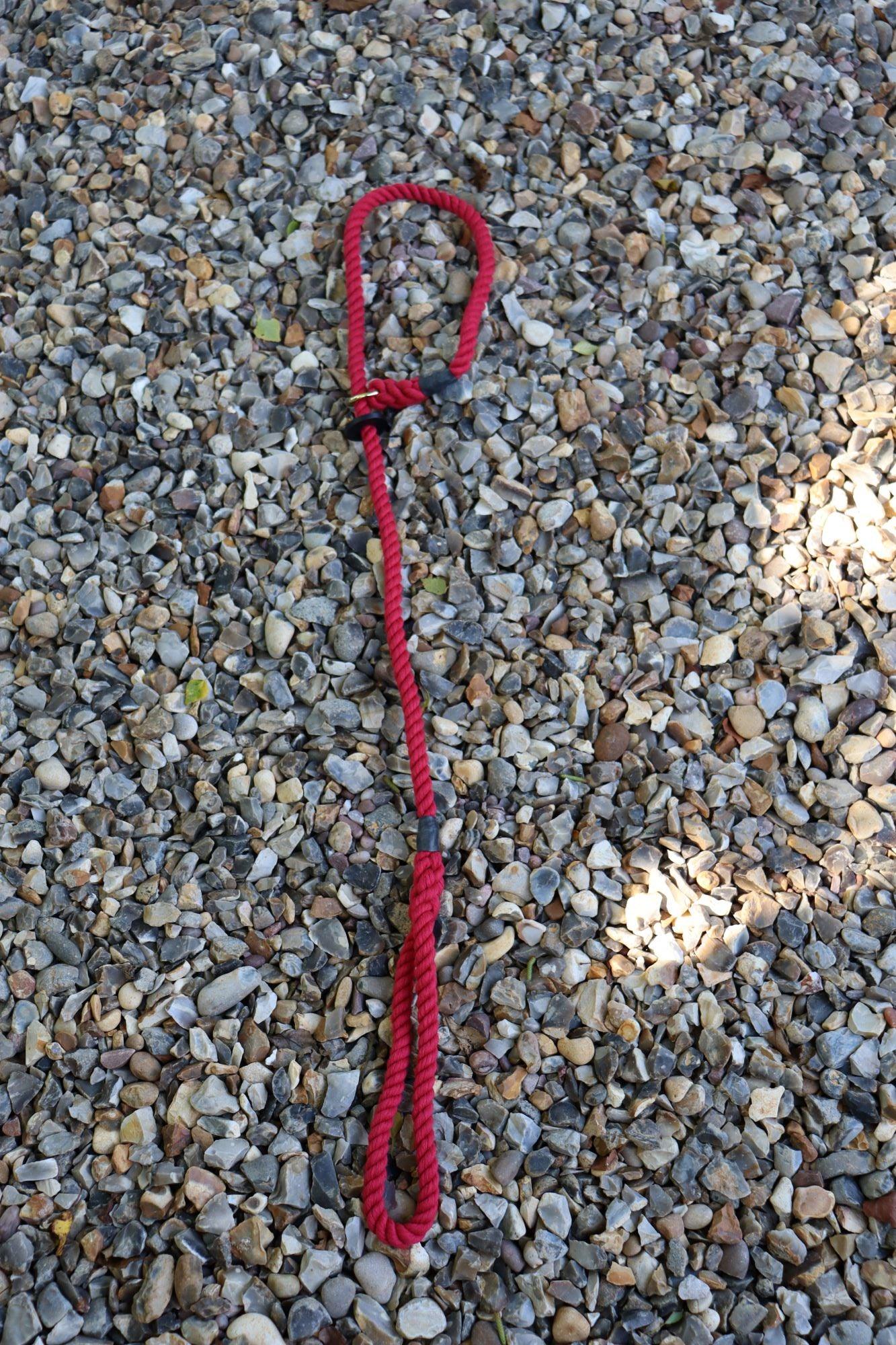 A raspberry slip lead stretched out along a stone path with the handle at the bottom and the loop at the top. You can clearly see the cotton spirals as a pattern and the lead has been hand spliced. There is a brass plated ring to complete the look for the collar loop.