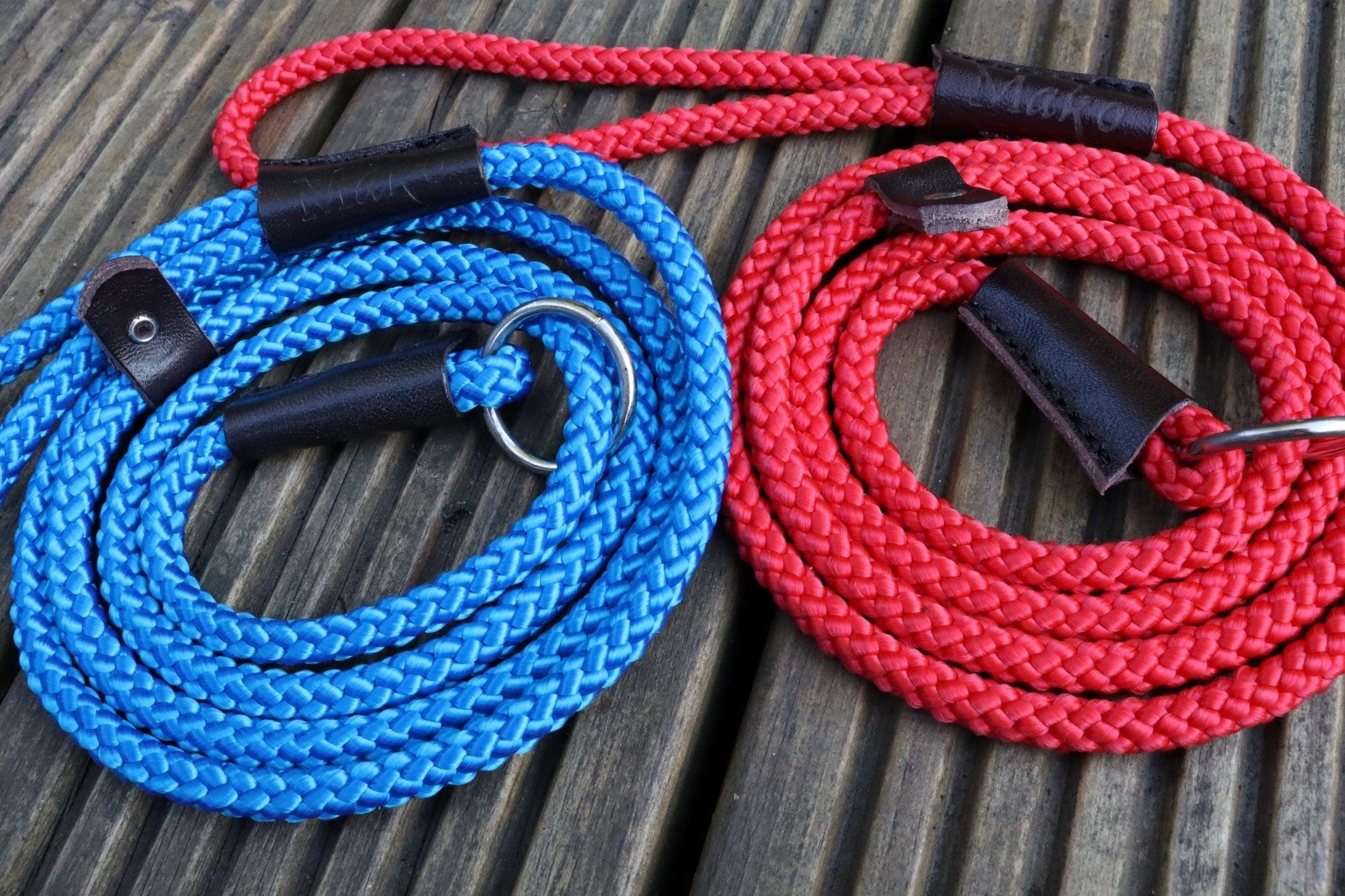 A close up on our red and our blue slip leads on wooden decking showing the detail of the braid and embossing on the handle.